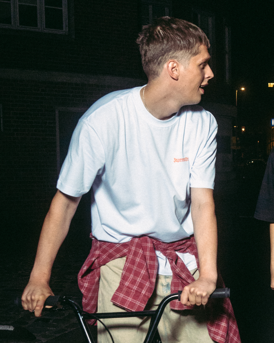 Persoon op een fiets ’s nachts, met een wit Jägermeister-T-shirt met een klein logo op de borst.