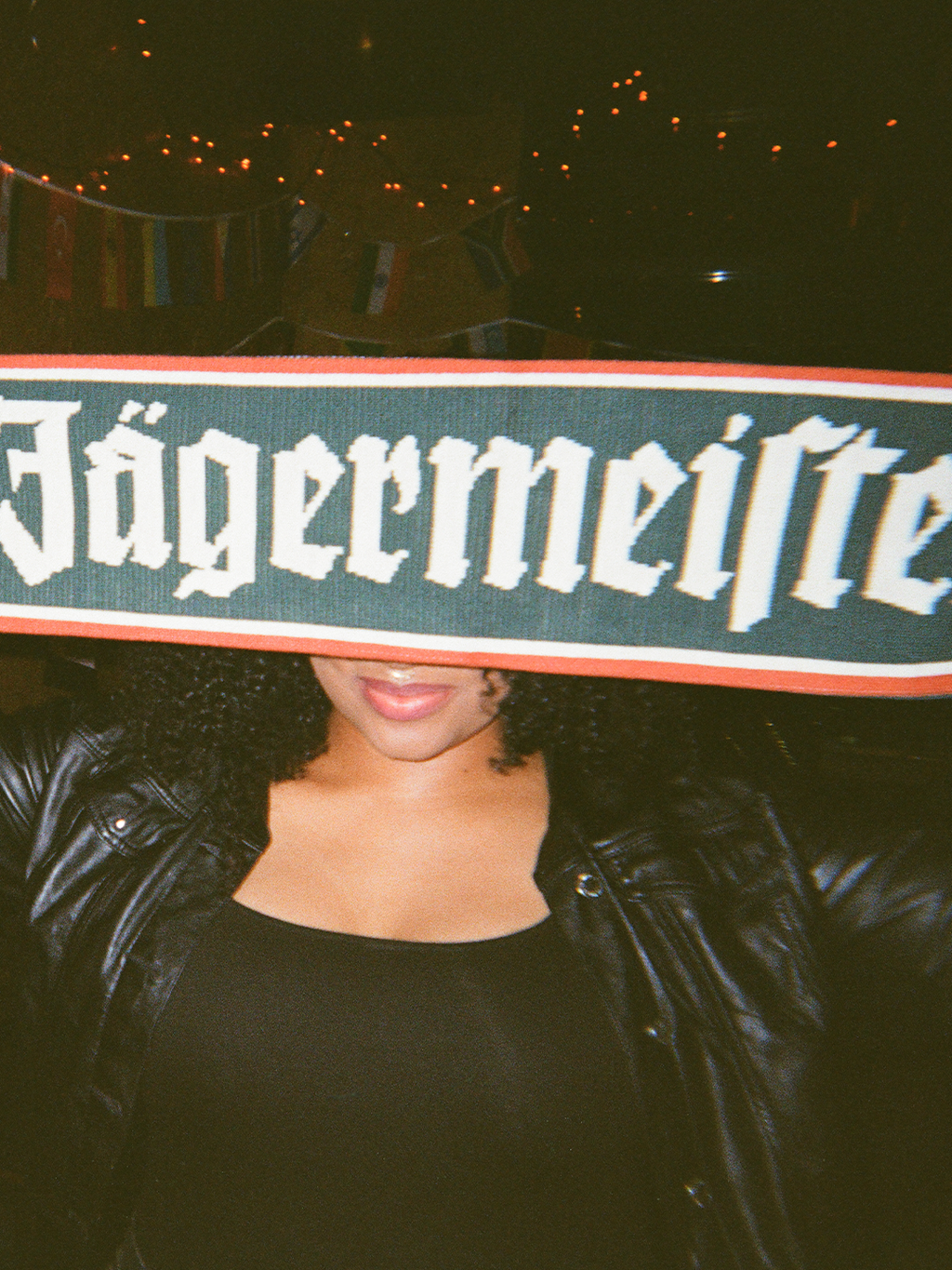 Persoon houdt een Jägermeister-sjaal voor zijn of haar gezicht met een donkere achtergrond.
