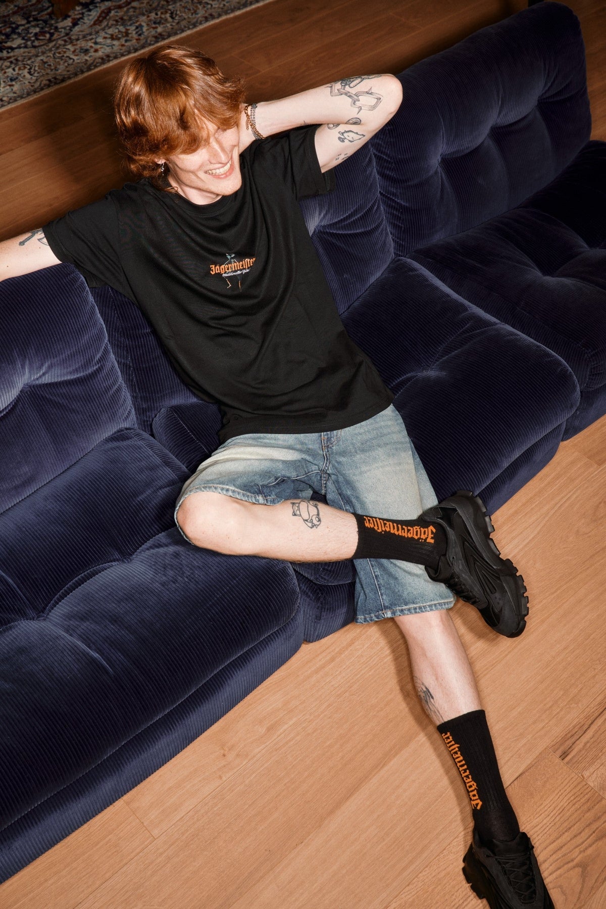 Person sitting on a blue couch wearing black socks with visible Jägermeister branding.