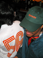 Twee mensen zitten samen in een barsfeer, waarvan één een groene Jägermeister dad cap draagt.