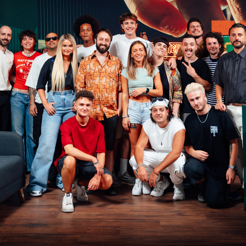 A group of twenty people posing together in a studio setting with a dark wood floor and a colorful graphic backdrop.