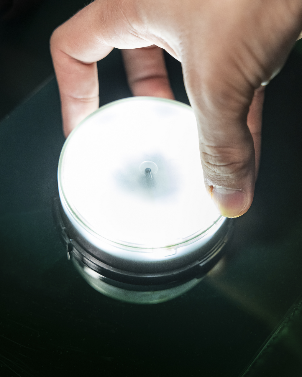 Hand die een kleine ronde lichtbron vasthoudt op een donkere ondergrond