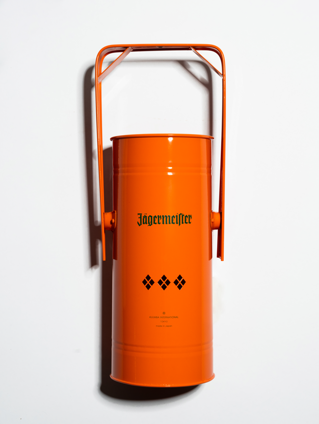 Oranje metalen wierookbrander met handvat en groen Jägermeister-logo op een witte achtergrond