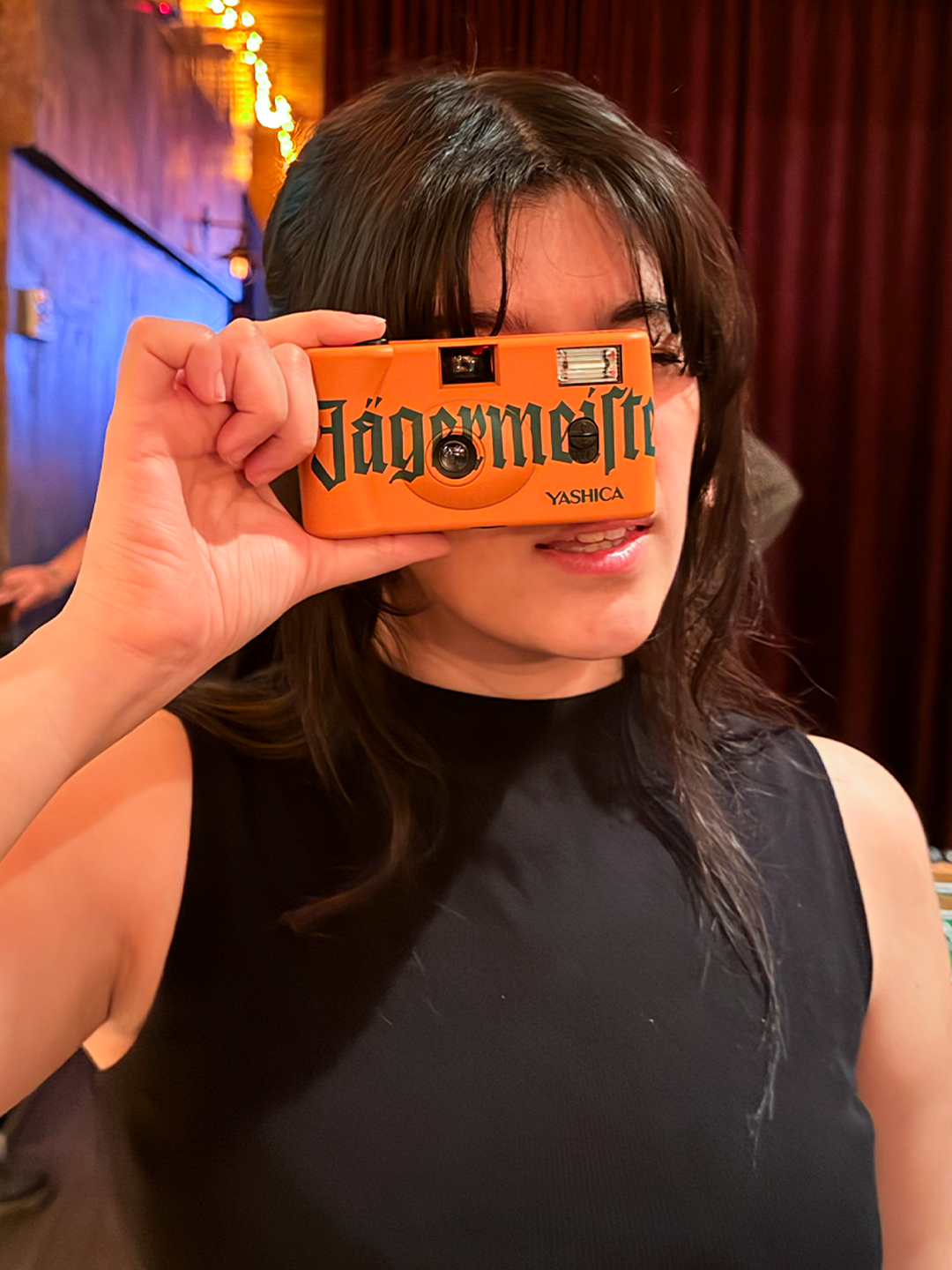 Persoon die een oranje camera met 'Jägermeister'-branding voor zijn gezicht houdt.