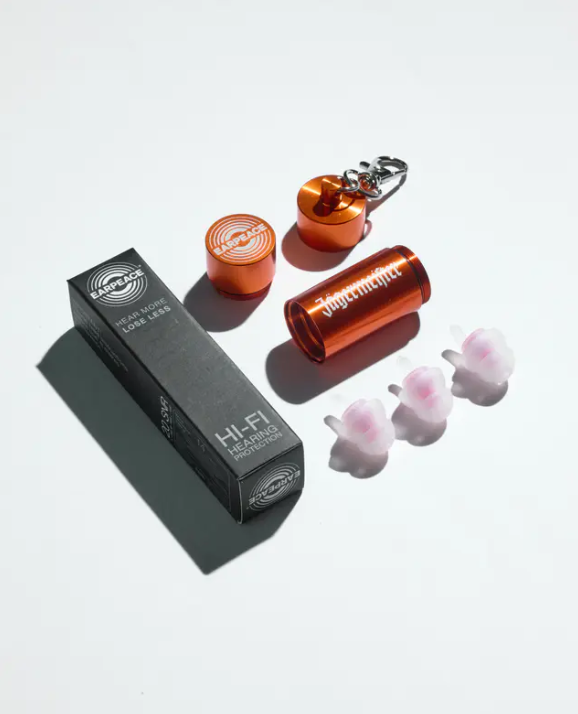 Drie oordoppen, een oranje metalen koker met daarop een witte Jägermeister-woordmarkering en een zwarte verpakkingsdoos op een witte achtergrond