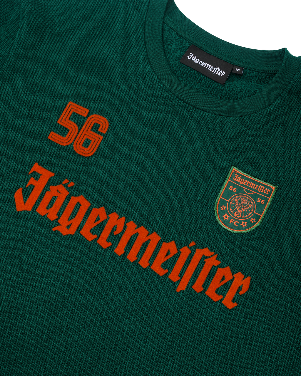 Groene Jägermeister-longsleeve met oranje Jägermeister-wordmark en een '56'.