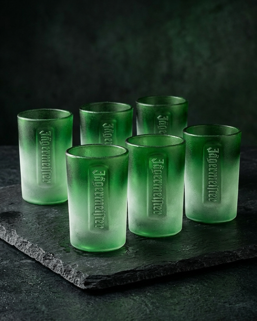 Set of six green shot glasses with embossed Jägermeister wordmark on a dark surface