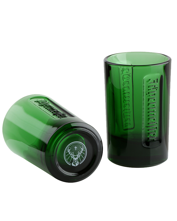 Two green Jägermeister glasses, one standing upright and one lying on its side, with embossed branding and the stag logo visible.