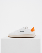 Een witte Jägermeister-sneaker met een feloranje hiellus en zwarte logotekst op de zijkant, tentoongesteld op een witte sokkel tegen een witte achtergrond.