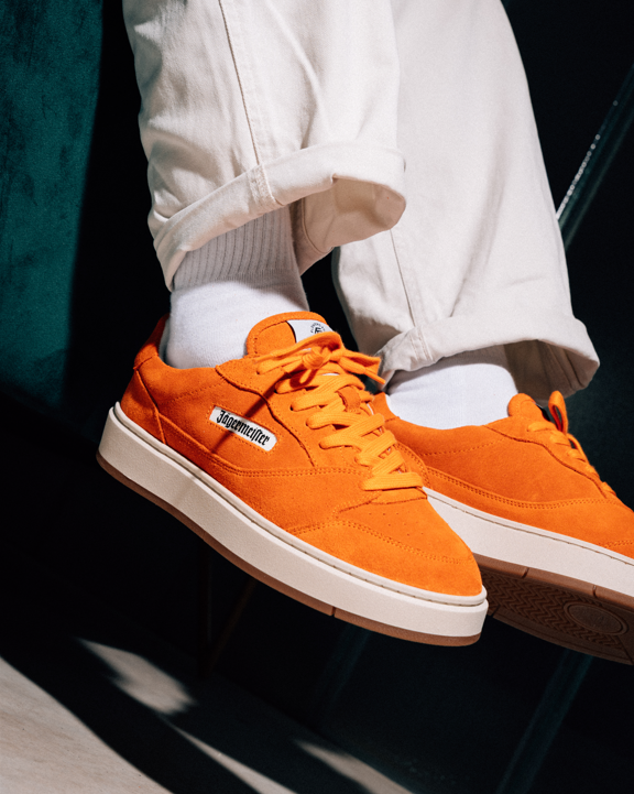 Feloranje Jägermeister sneakers met witte zolen en witte sokken, gedragen met crèmekleurige omgeslagen broek, gepresenteerd in een gestylede lifestyle-setting.
