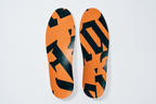Een paar inlegzolen voor sportschoenen met een Jägermeister-oranje en zwart patroon, van bovenaf gezien op een lichte achtergrond.