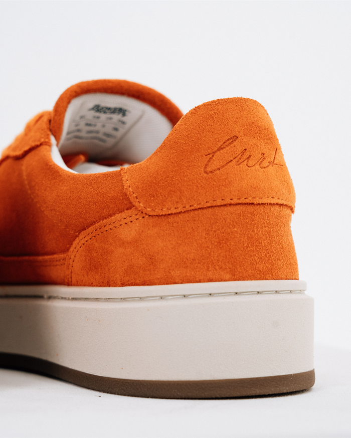 Close-up achteraanzicht in driekwart van een oranje Jägermeister sneaker met een dikke gebrokenwitte plateauzool en bruine buitenzool, met het hielstuk met geborduurde naam 'Curt'