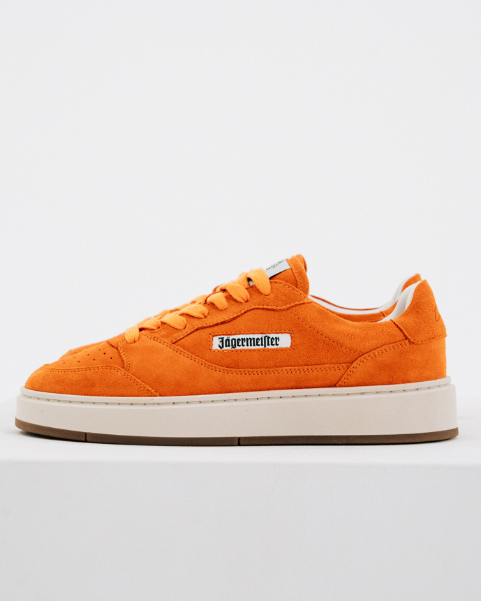 Een oranje Jägermeister sneaker met een dikke crèmekleurige plateauzool en een wit zijlabel met 'Jägermeister'.