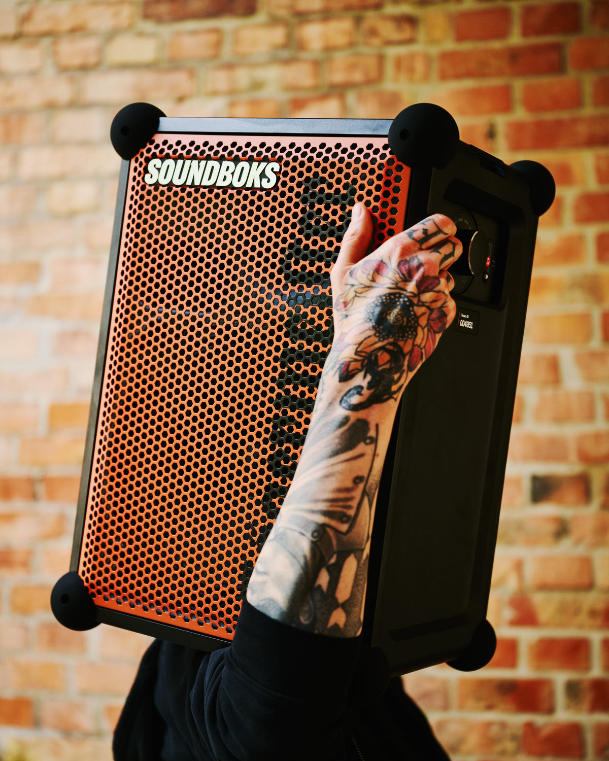 Person holding a Soundboks speaker against a brick wall